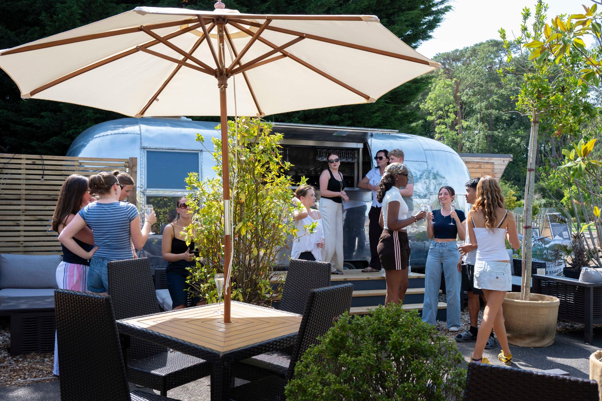 Guests enjoying drinks under a parasol in the Courtyard at The Glasshouse restaurant, Windlesham, with the Airstream bar behind